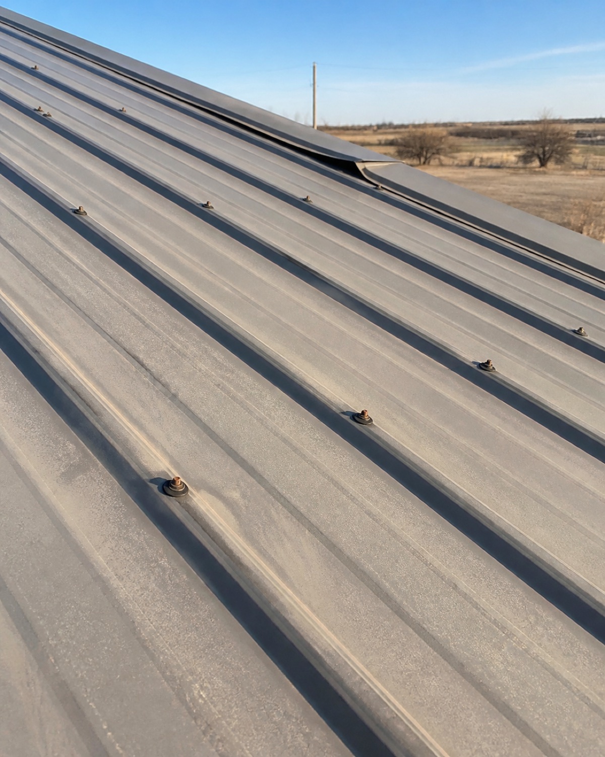 Aged washers, slight oxidation, and loose trim on an older exposed-fastener metal roof