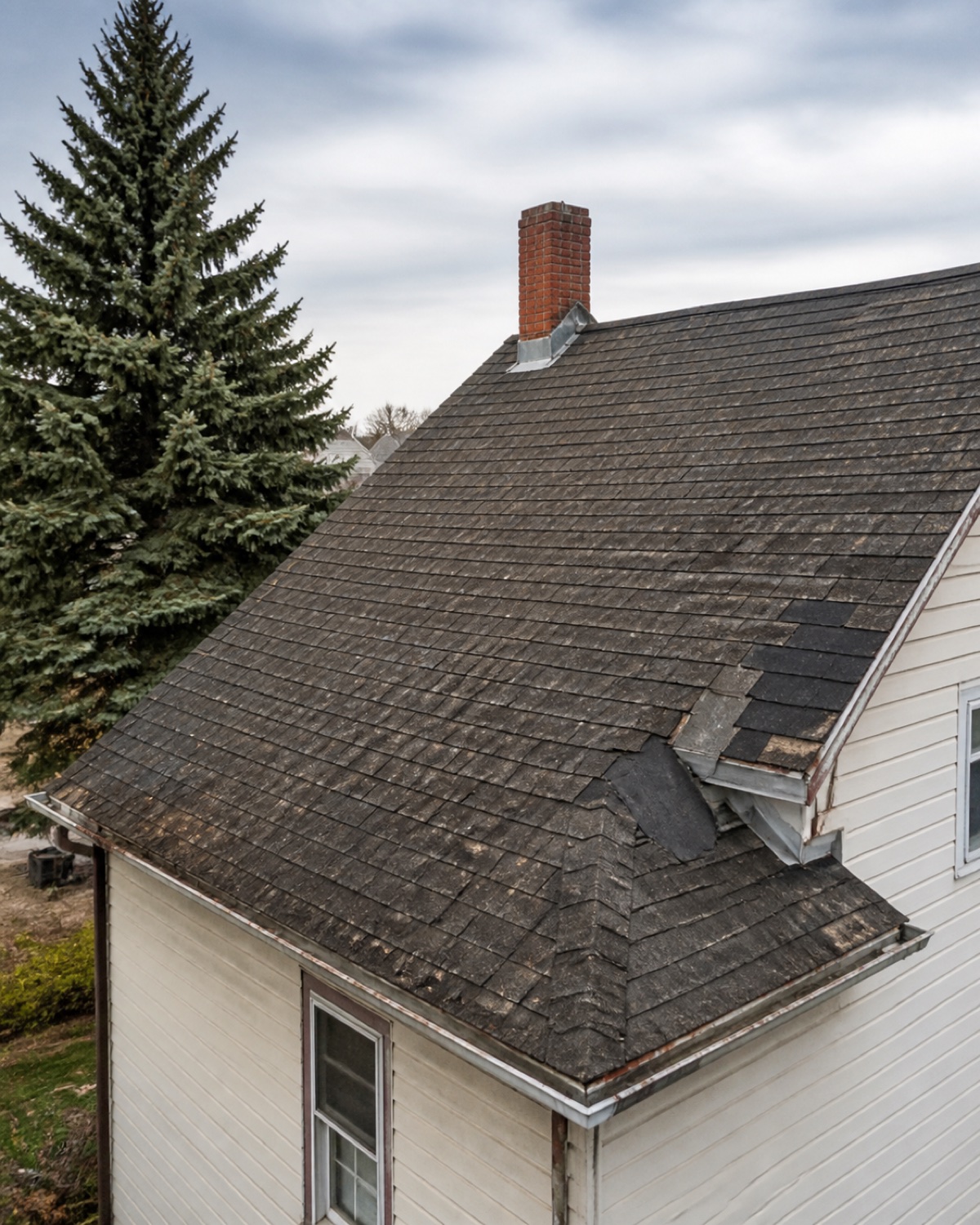 Aging asphalt roof with curling edges, granule wear, and older patches
