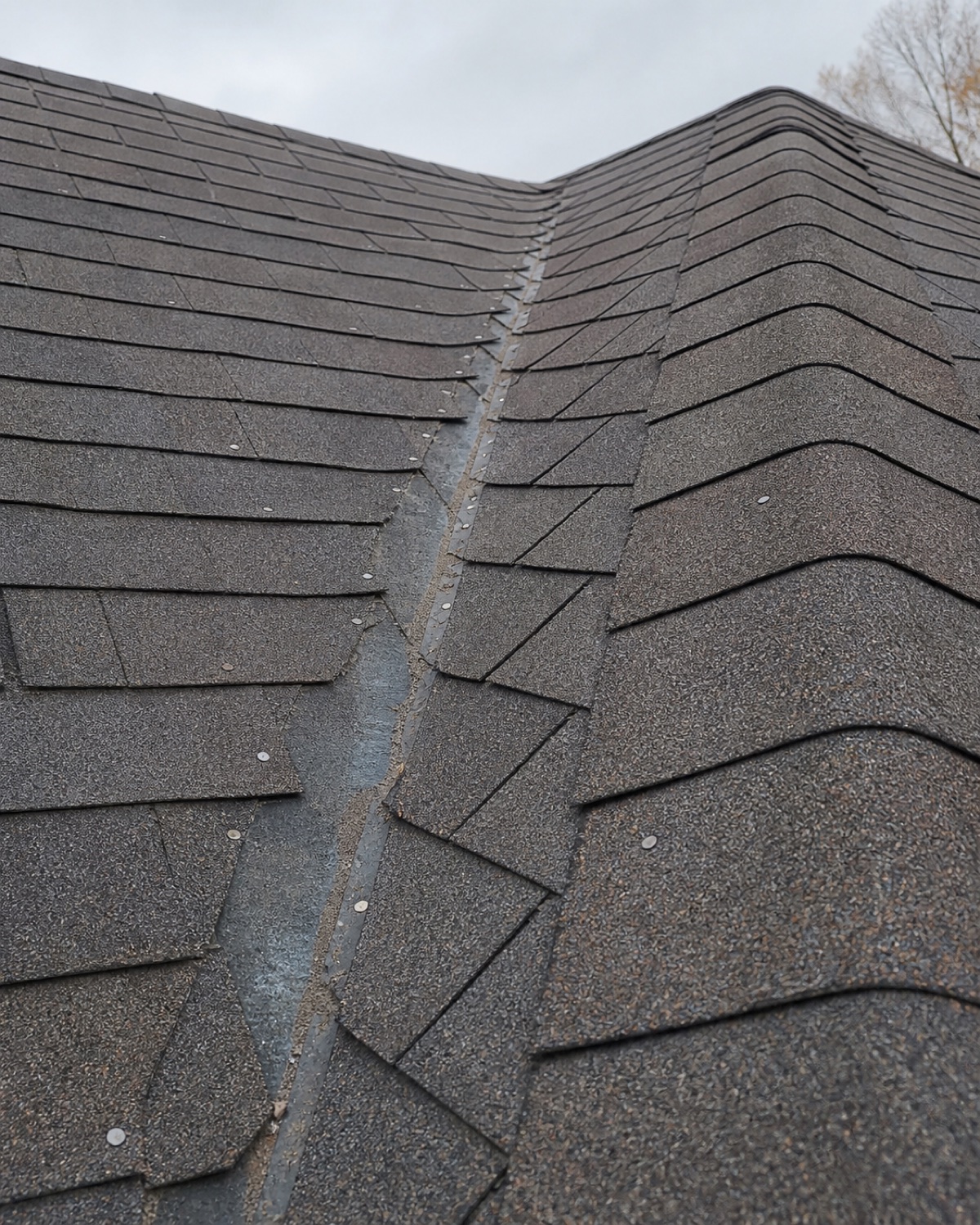 Uneven shingles, exposed fasteners, and a poorly cut valley on a roof needing correction